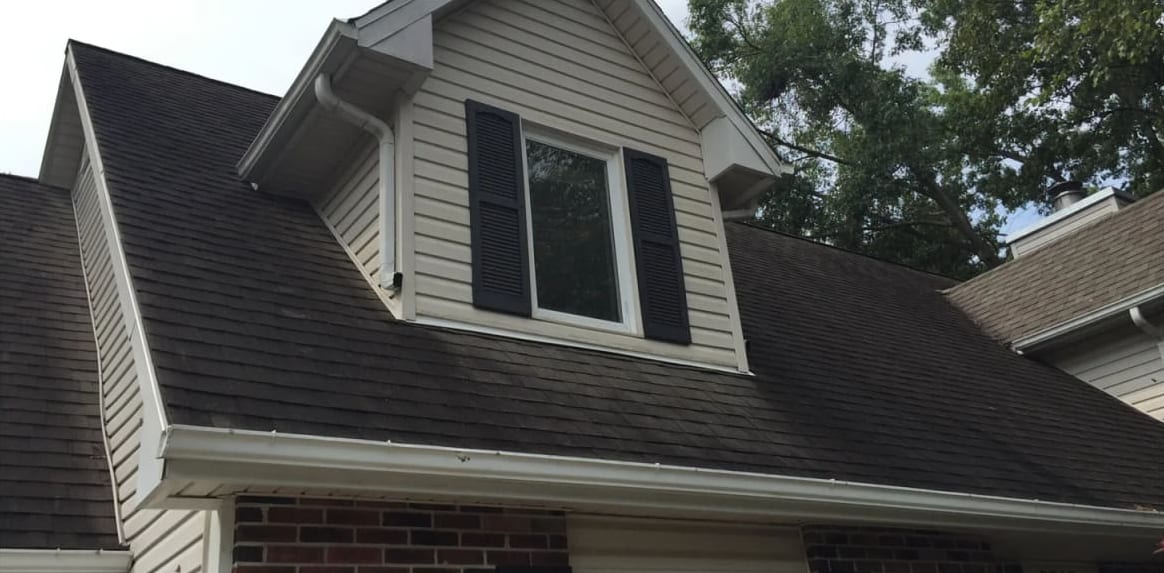 Shingle roof and dormer dark with black algae streaks before soft wash roof cleaning in Jefferson City, MO